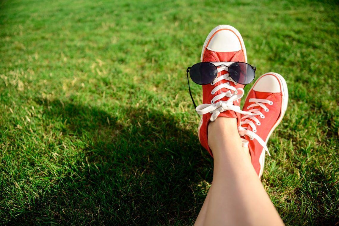 Close up photo of girl's legs in red keds lying on grass. Copy space.
