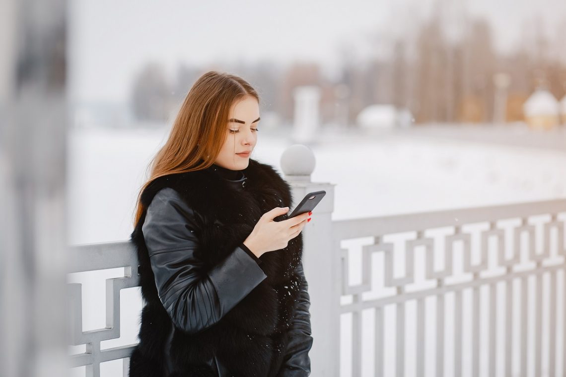 Cute girl standing in a winter park. Woman with mobile phone