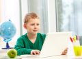 Portrait of smart schoolboy typing on laptop at lesson